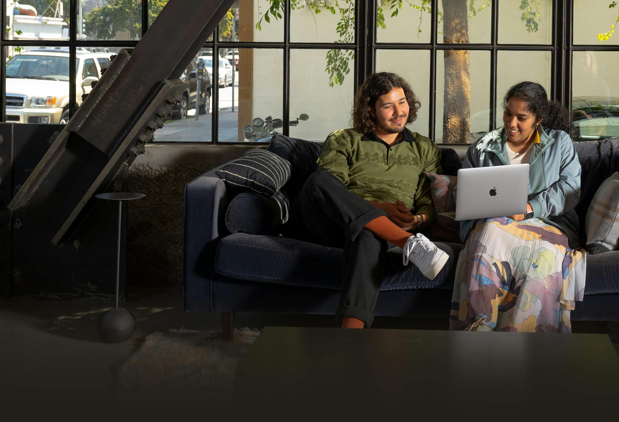 Two Watershed employees sitting on a couch at the San Francisco office, happily looking at a laptop